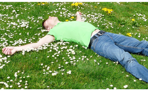 man in green shirt lying on field with dandelion