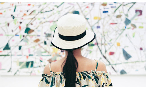 lady in white hat with black trimming looking at painting with white background