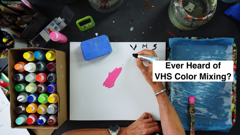 Top-down view of an art desk with paint bottles, brushes, and a hand writing on a white sheet; bold overlay reads 'Ever Heard of VHS Color Mixing?'