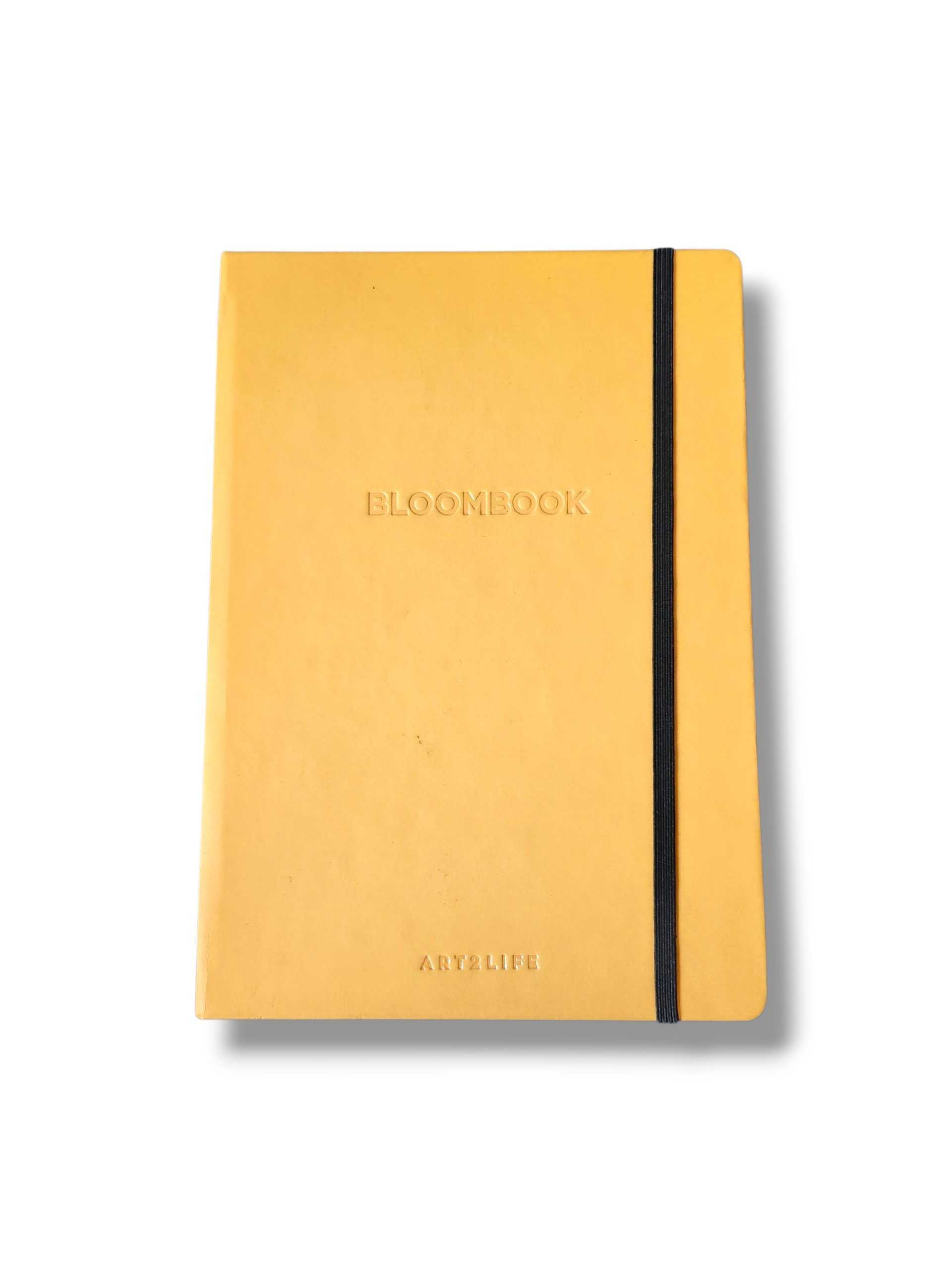 Yellow hardcover notebook with a black elastic strap running along the right edge, embossed with BLOOMBOOK on the cover.