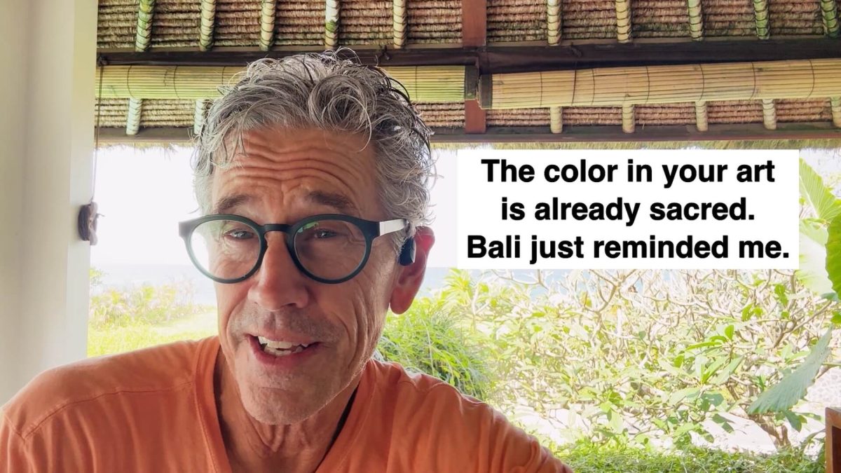Selfie of an older man with gray hair and teal glasses outdoors, with a large white caption reading: 'The color in your art is already sacred. Bali just reminded me.'