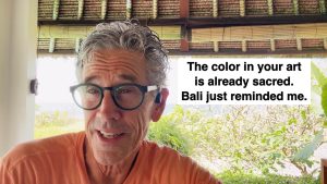 Selfie of an older man with gray hair and teal glasses outdoors, with a large white caption reading: 'The color in your art is already sacred. Bali just reminded me.'