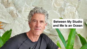 Man with gray hair in a black striped shirt in front of a stone wall, caption reads 'Between My Studio and Me Is an Ocean'.